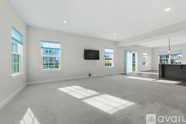 A spacious living room with a flat-screen TV mounted on the wall and large windows allowing natural light to enter.