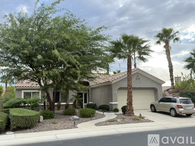 A house with a car parked in front and palm trees in the background.