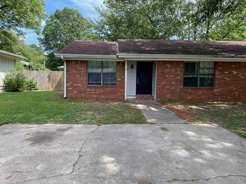 A small brick house with a white door and a white fence.