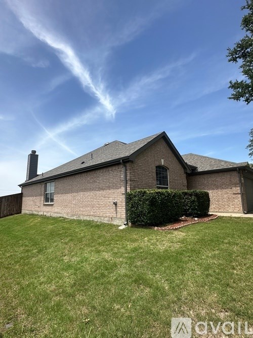 A house with a grey roof and a chimney is surrounded by a green lawn.