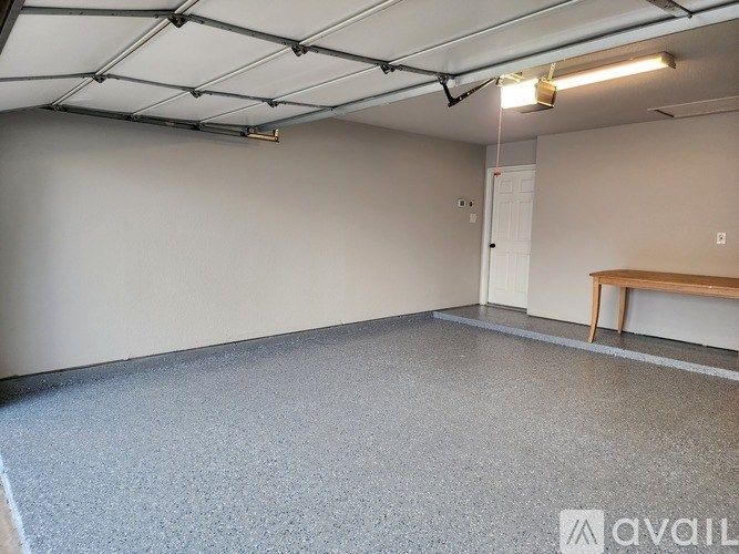 A room with a grey floor and a white wall with a door and a bench.