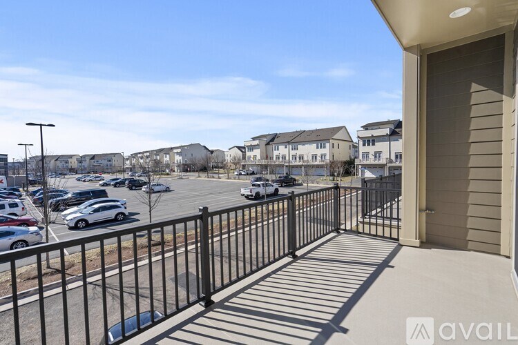 A balcony with a black railing overlooks a parking lot and buildings.
