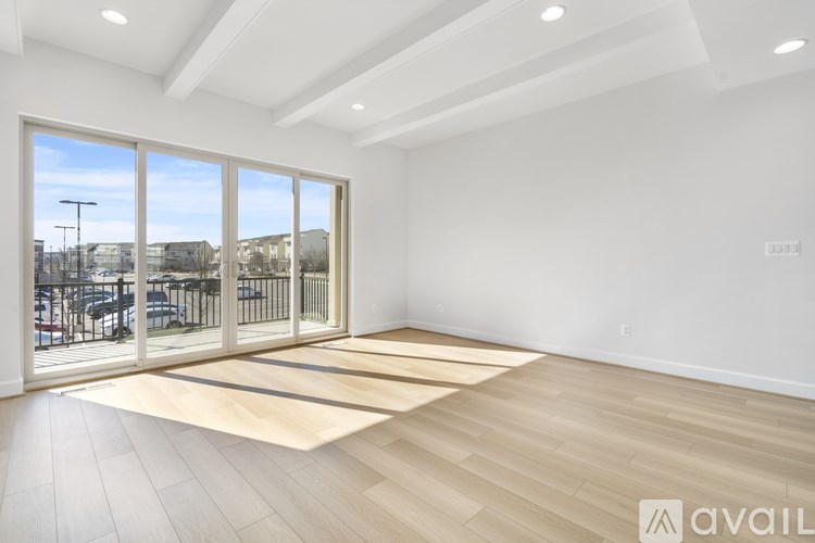 A spacious room with wooden flooring and a large window overlooking a patio.