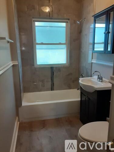 A bathroom with a tub, toilet, sink, and a window.