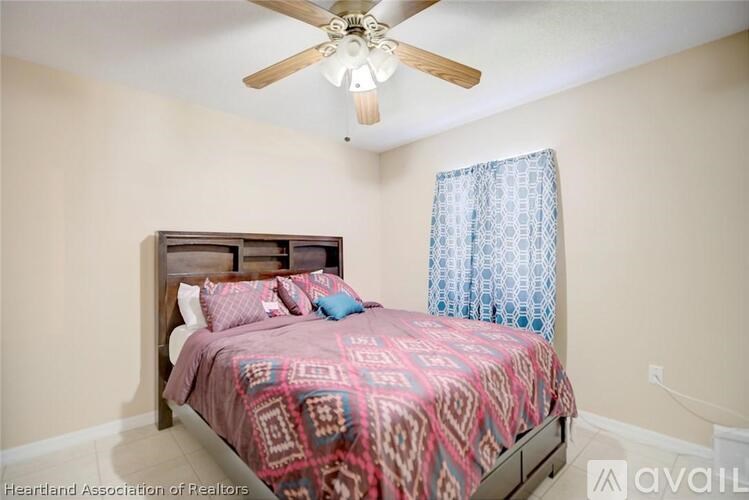 A bedroom with a bed, pillows, a ceiling fan, and a window with a curtain.