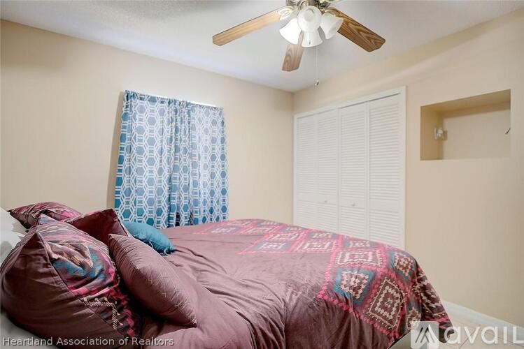 A bedroom with a bed, pillows, a ceiling fan, and a window with a curtain.