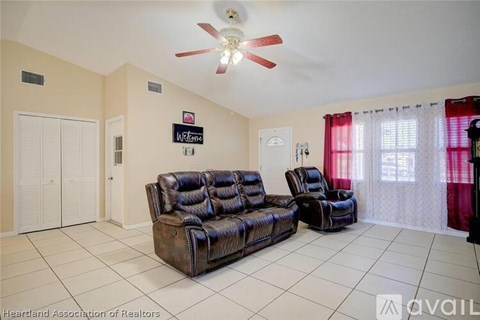 A living room with a black leather couch and a fan on the ceiling.