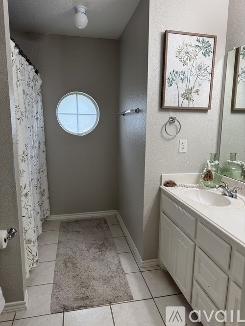 A bathroom with a round window and a framed picture on the wall.