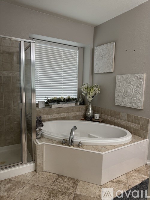 A bathroom with a tub, a window with blinds, and a wall hanging.