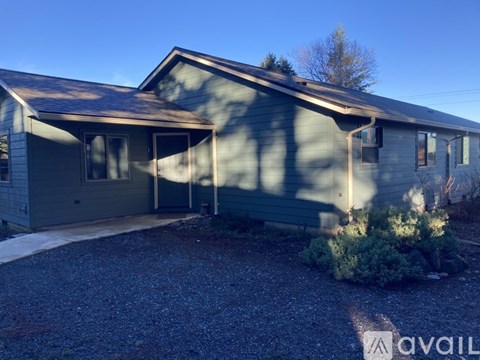 A house with a gravel driveway and a tree in the background.