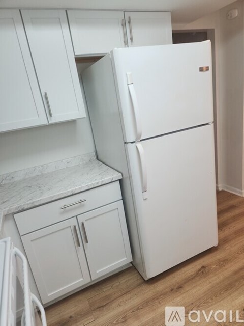 A white refrigerator stands next to a white countertop with cabinets.