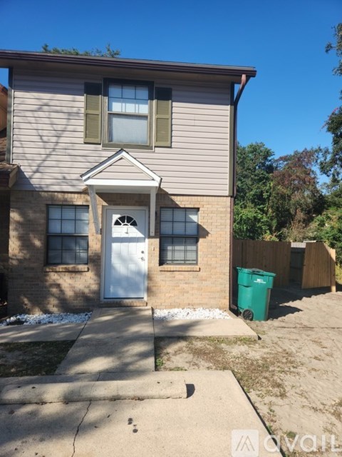 A house with a white door and a green trash bin in front.