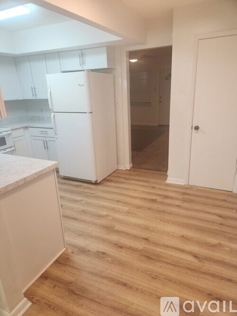 A kitchen with white appliances and cabinets with a wooden floor.