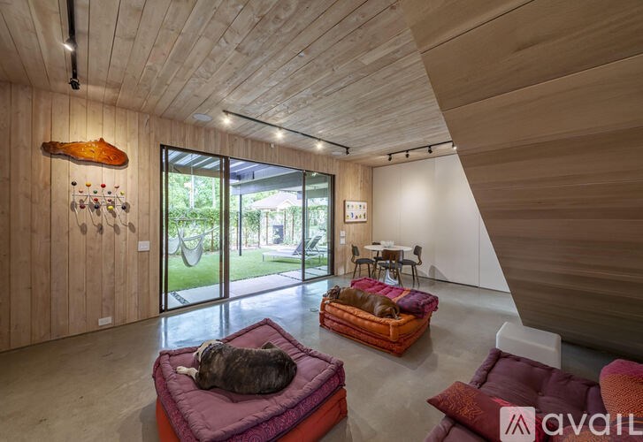 A cat is lying on a pink cushion in a room with wooden walls and ceiling.