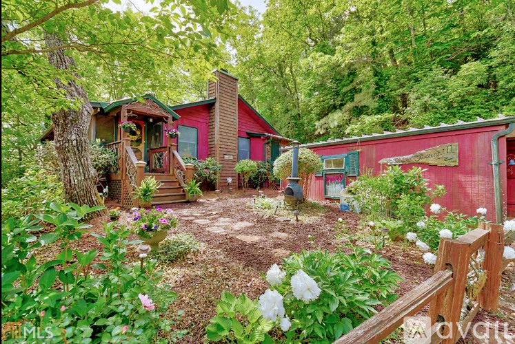 A red house with a wooden deck and a garden in front.