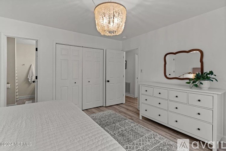 A bedroom with a large bed, a chandelier, and a white dresser.