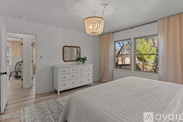 A bedroom with a large bed, a dresser, and a window with curtains.