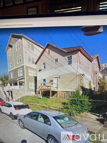 A grey car is parked in front of a two-story house.