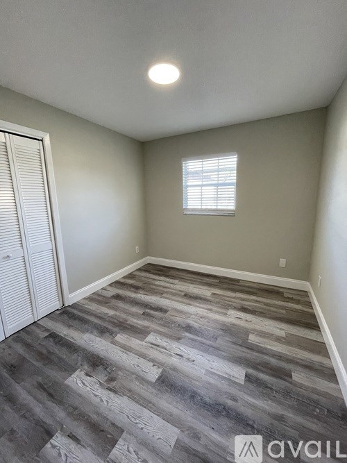 A room with a grey wood floor and a window with blinds.