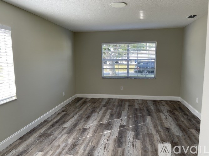 A room with wooden flooring and a window showing a parking lot outside.