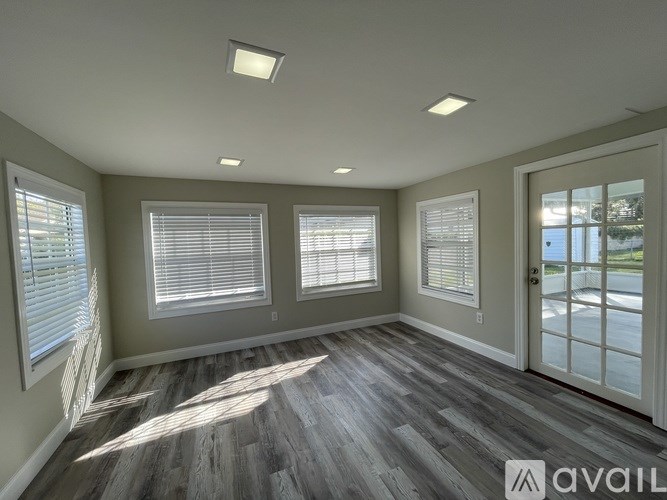 A room with wooden flooring and three windows with blinds.