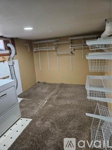 A kitchen area with a refrigerator, a floor with a carpet, and a wall with a pipe.