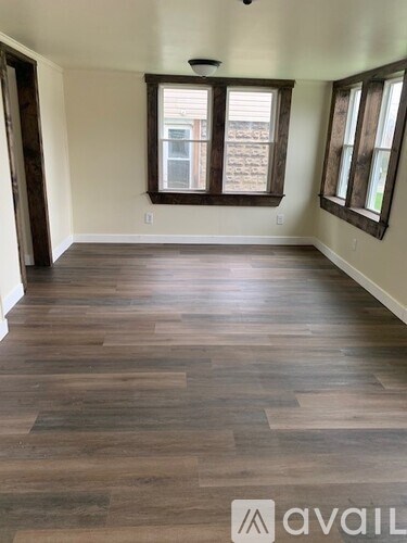 A room with wooden flooring and two windows.