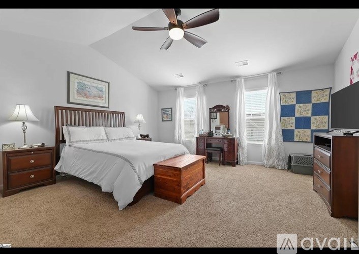 A bedroom with a large bed, a ceiling fan, and a window with curtains.