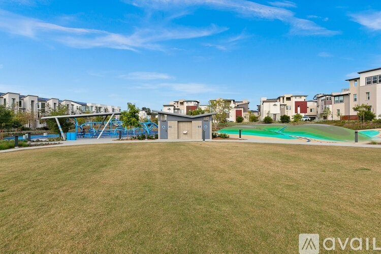 A grassy field with a playground and buildings in the background.