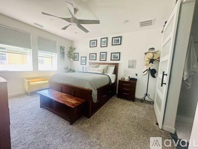 A bedroom with a bed, a bench, a ceiling fan, and pictures on the wall.
