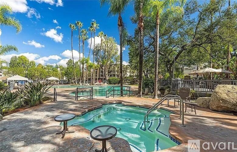 A pool surrounded by palm trees and a patio area with chairs and a table.