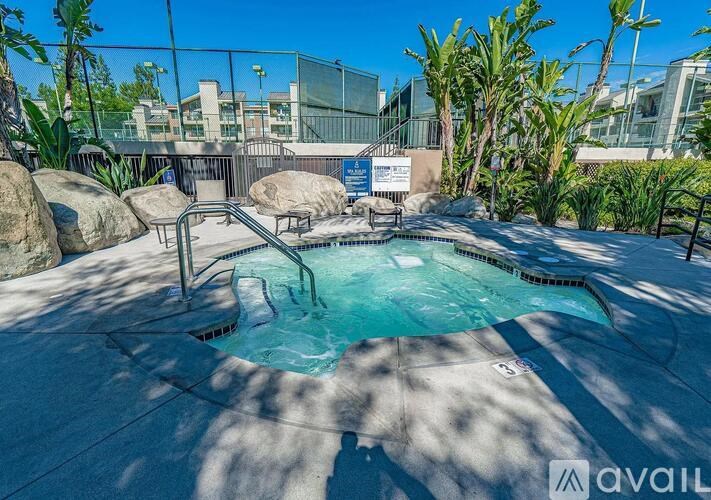 A hot tub is surrounded by rocks and palm trees.