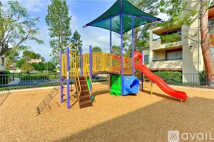 A playground with a red slide, a green canopy, and a yellow and purple structure.