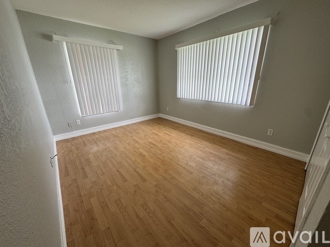 A room with wooden flooring and two windows with blinds.