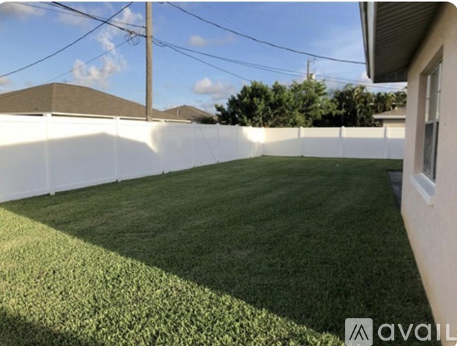A backyard with a white fence and green grass.