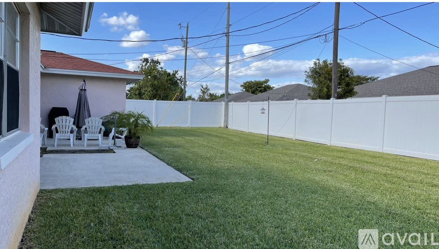 A backyard with a white fence and a patio with chairs and an umbrella.