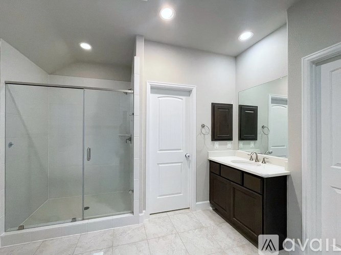 A bathroom with a walk-in shower, double sink vanity, and a white door.