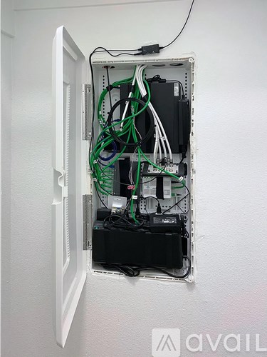 A white door is open to reveal a rack with many cables and a black box.