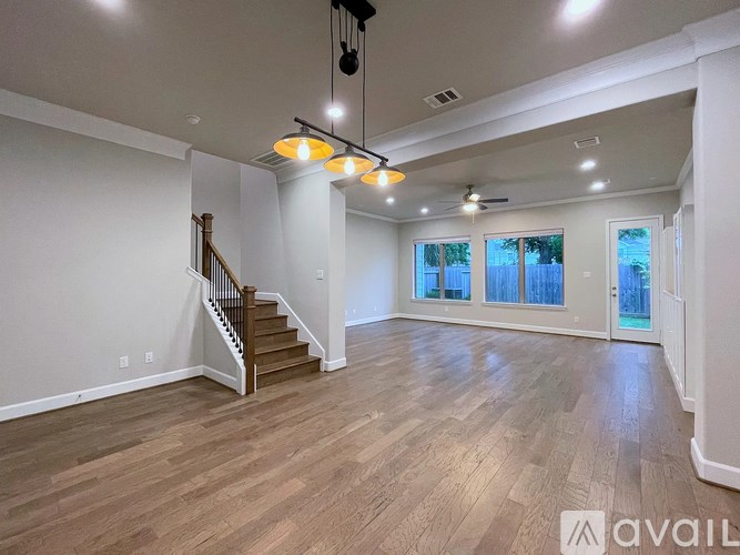A spacious room with wooden flooring and a staircase.