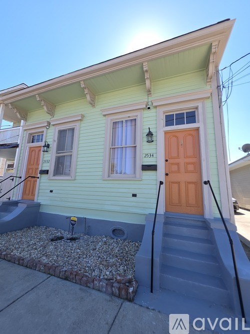 A yellow house with a brown door and a staircase leading to the front door.