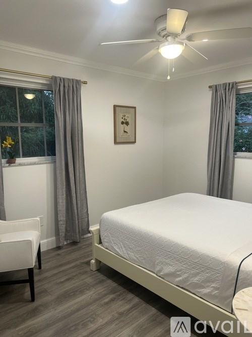 A bedroom with a bed, chair, and window with curtains.