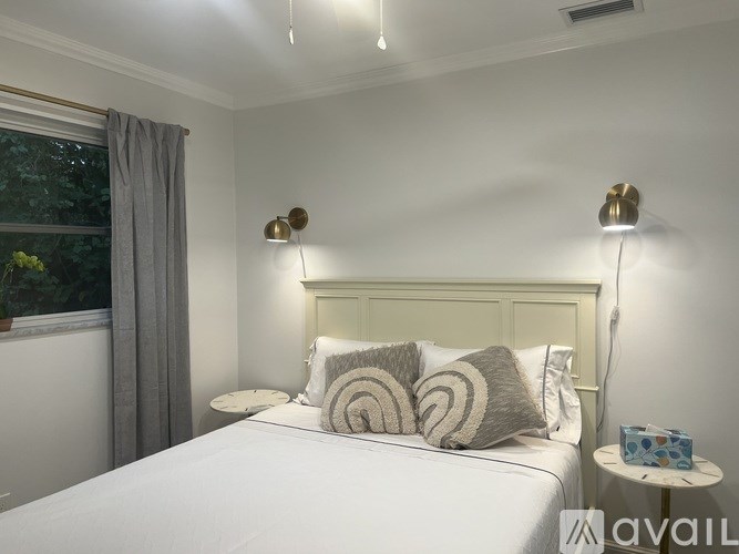 A bedroom with a white bed and a window with grey curtains.