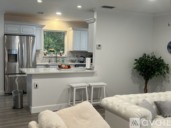 A white kitchen with a refrigerator, sink, and bar stools.