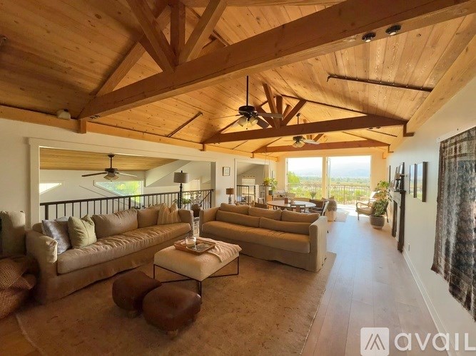 A spacious living room with wooden beams on the ceiling and a large window.