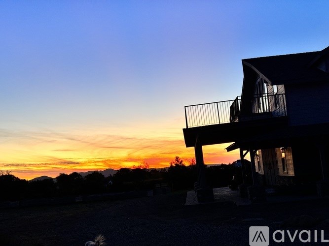 A house with a balcony is silhouetted against a sunset sky.