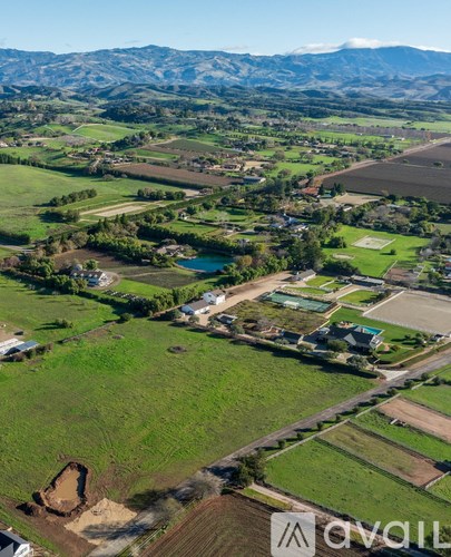 A rural landscape with a large field, a lake, and mountains in the distance.