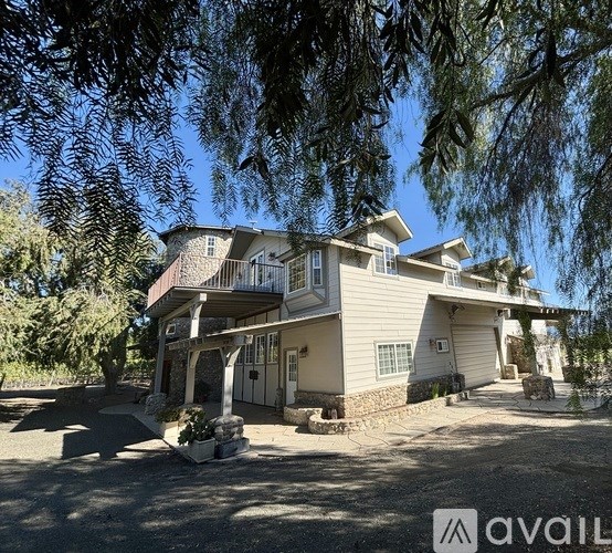 A house with a balcony and a stone wall is surrounded by trees.