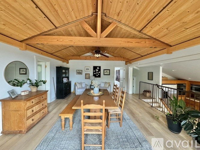 A wooden table with chairs and a potted plant sits in the middle of a room with a wooden ceiling.
