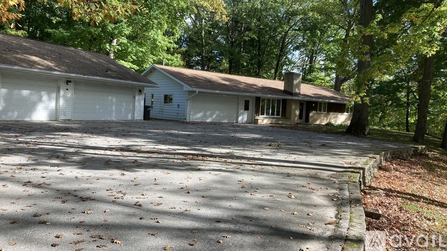 A house with a driveway in front of it surrounded by trees.