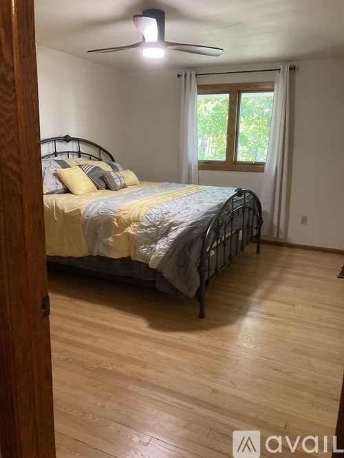A bedroom with a bed, wooden floor, and a ceiling fan.